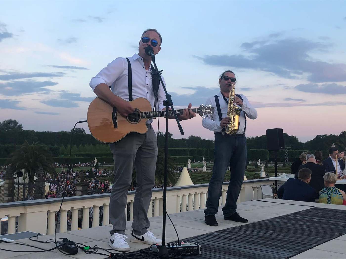 John Eid und ein Saxophonist spielen gemeinsam bei einem Abendevent auf einer Dachterrasse