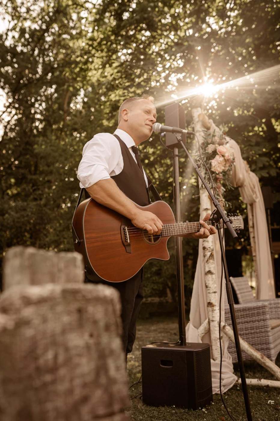 John Eid singt und spielt akustische Gitarre bei einer Trauung im Freien, goldenes Abendlicht